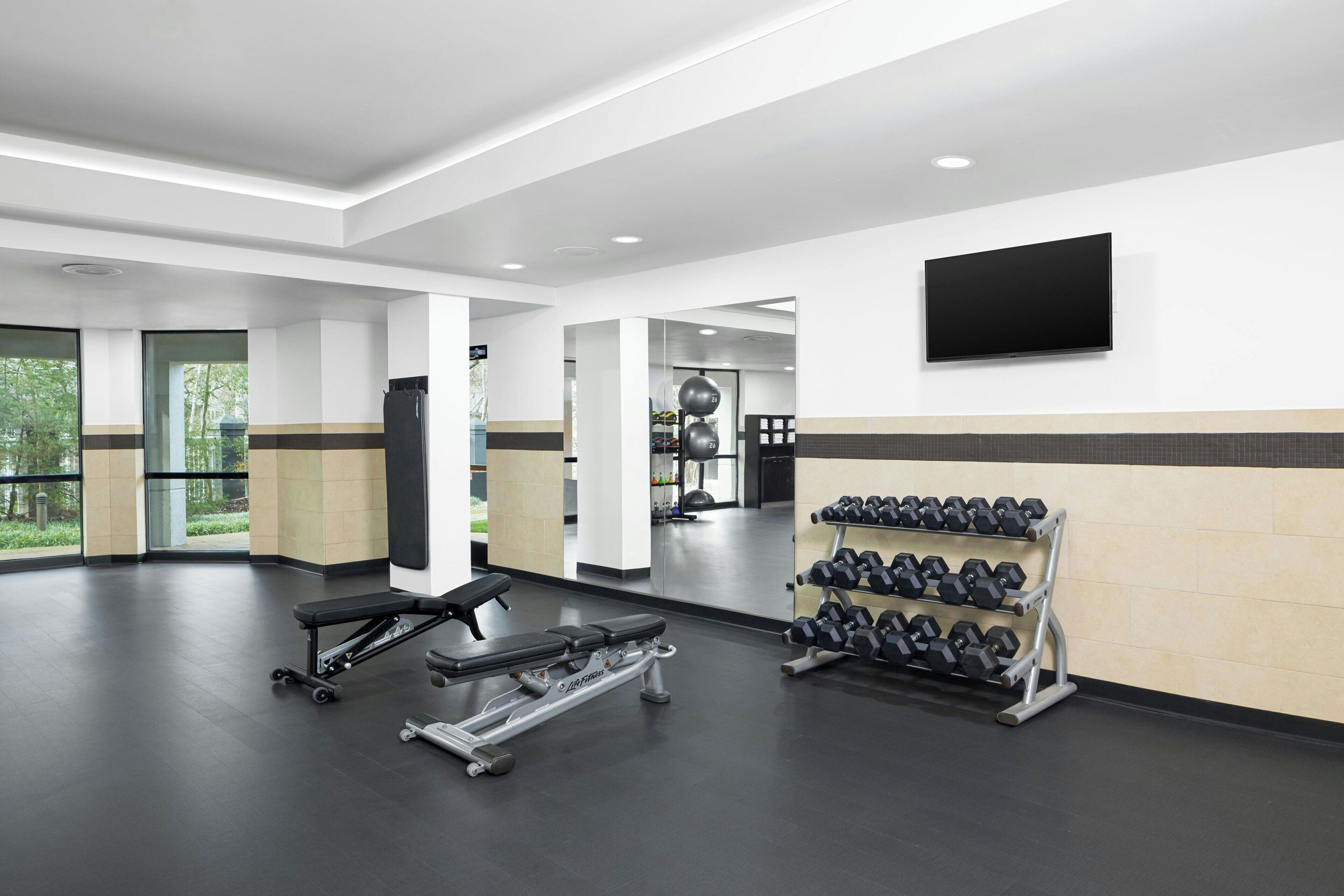 Un gimnasio moderno con una prensa de banca, mancuernas y un televisor en la pared.