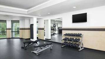 Un gimnasio moderno con una prensa de banca, mancuernas y un televisor en la pared.