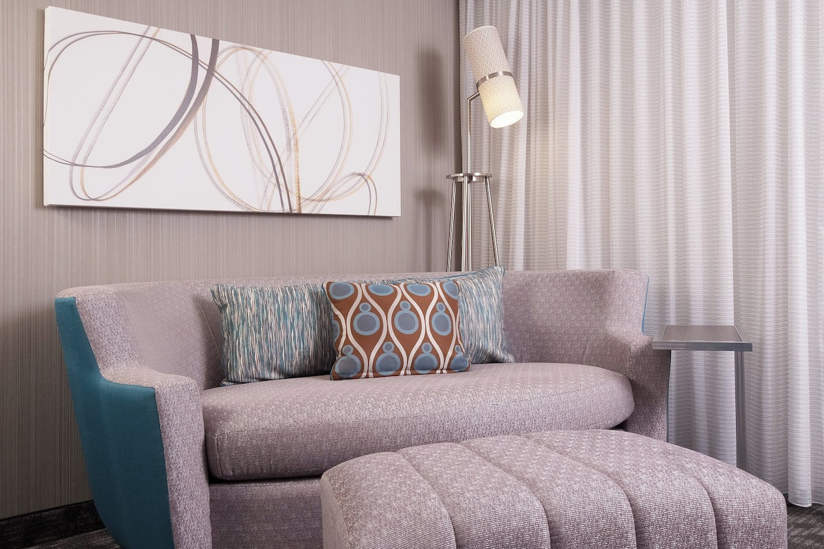 Un salon moderne avec un canapé gris, un pouf à motifs et une lampe sur pied.
