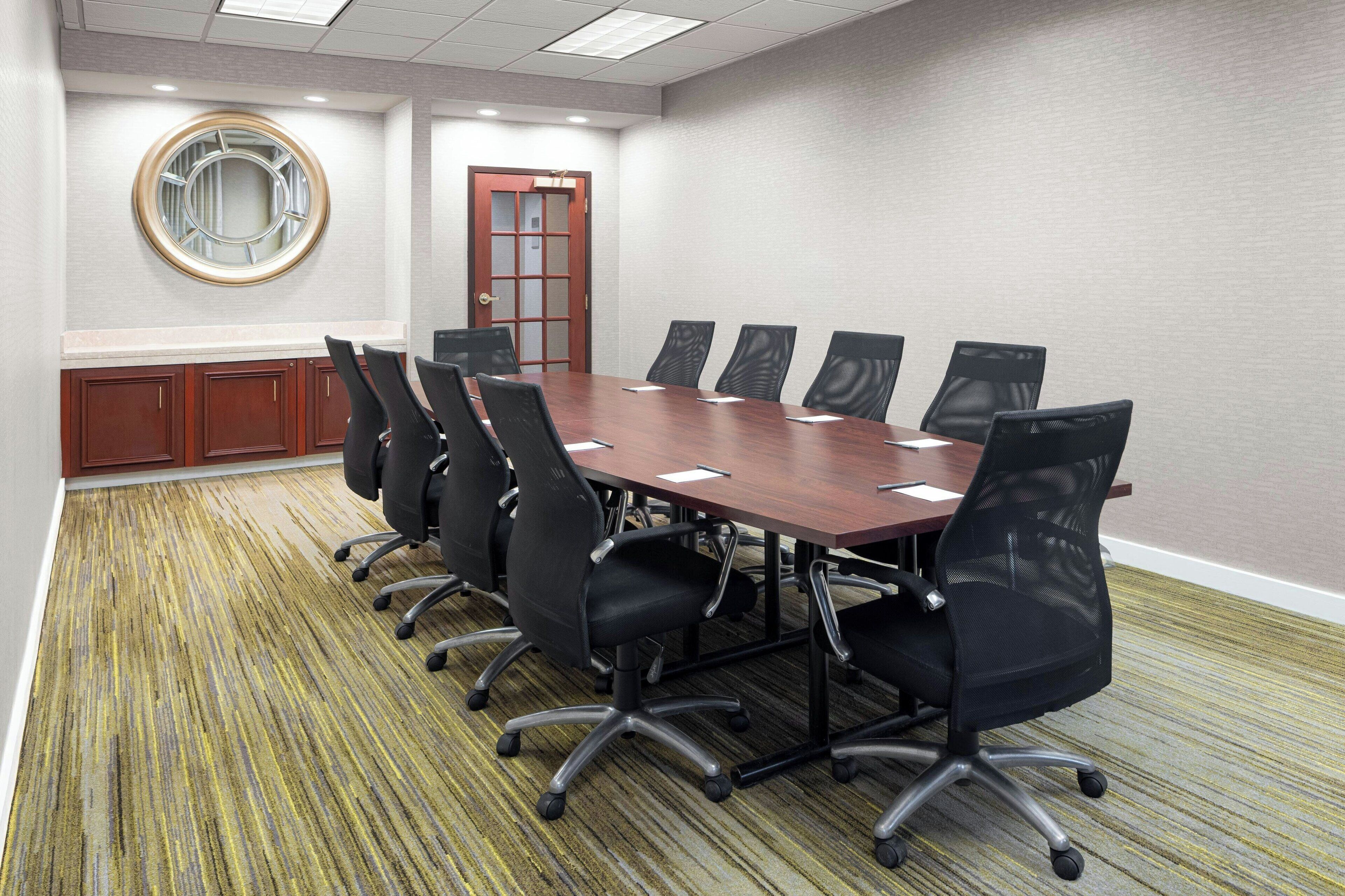 Une salle de conférence avec une longue table, six chaises, un buffet en bois et une porte dotée de panneaux en verre dépoli.
