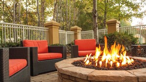 An outdoor seating area with wicker furniture and red cushions, surrounded by a stone fire pit.