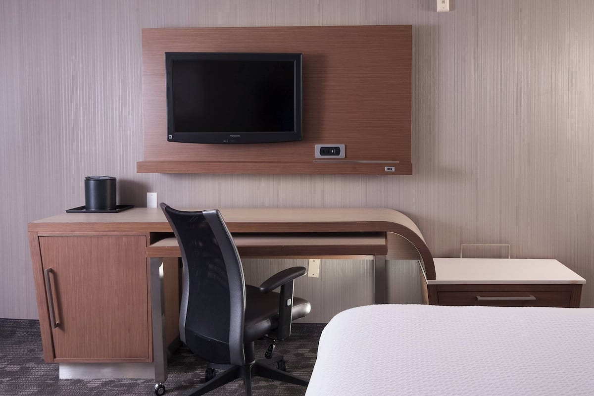 Une chambre d’hôtel comprenant un lit, un bureau avec une chaise, un téléviseur fixé au mur et une petite table.