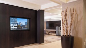 A modern lobby with a large screen displaying a cityscape, a dark wooden reception desk, and a tall vase with branches.
