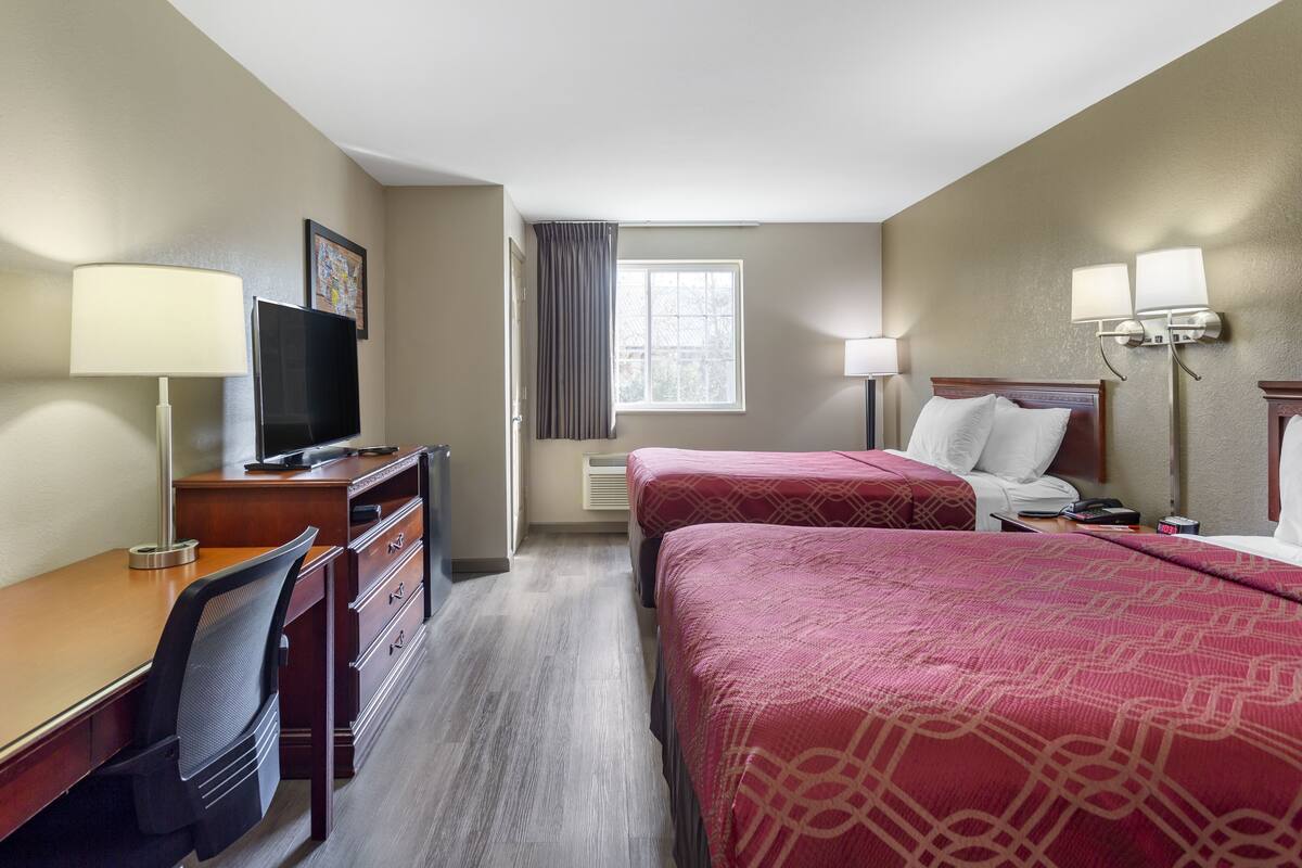 Une chambre d’hôtel avec deux lits, un bureau, une chaise, une télévision et une fenêtre avec des rideaux.