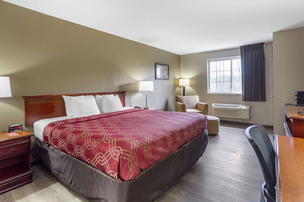 Une chambre d’hôtel comprenant un lit, des tables de chevet, un bureau, une chaise, une lampe, une fenêtre avec des rideaux et un téléviseur fixé au mur.