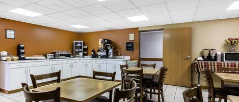 Un comedor con mostrador de cocina, máquinas de café y una mesa de buffet.