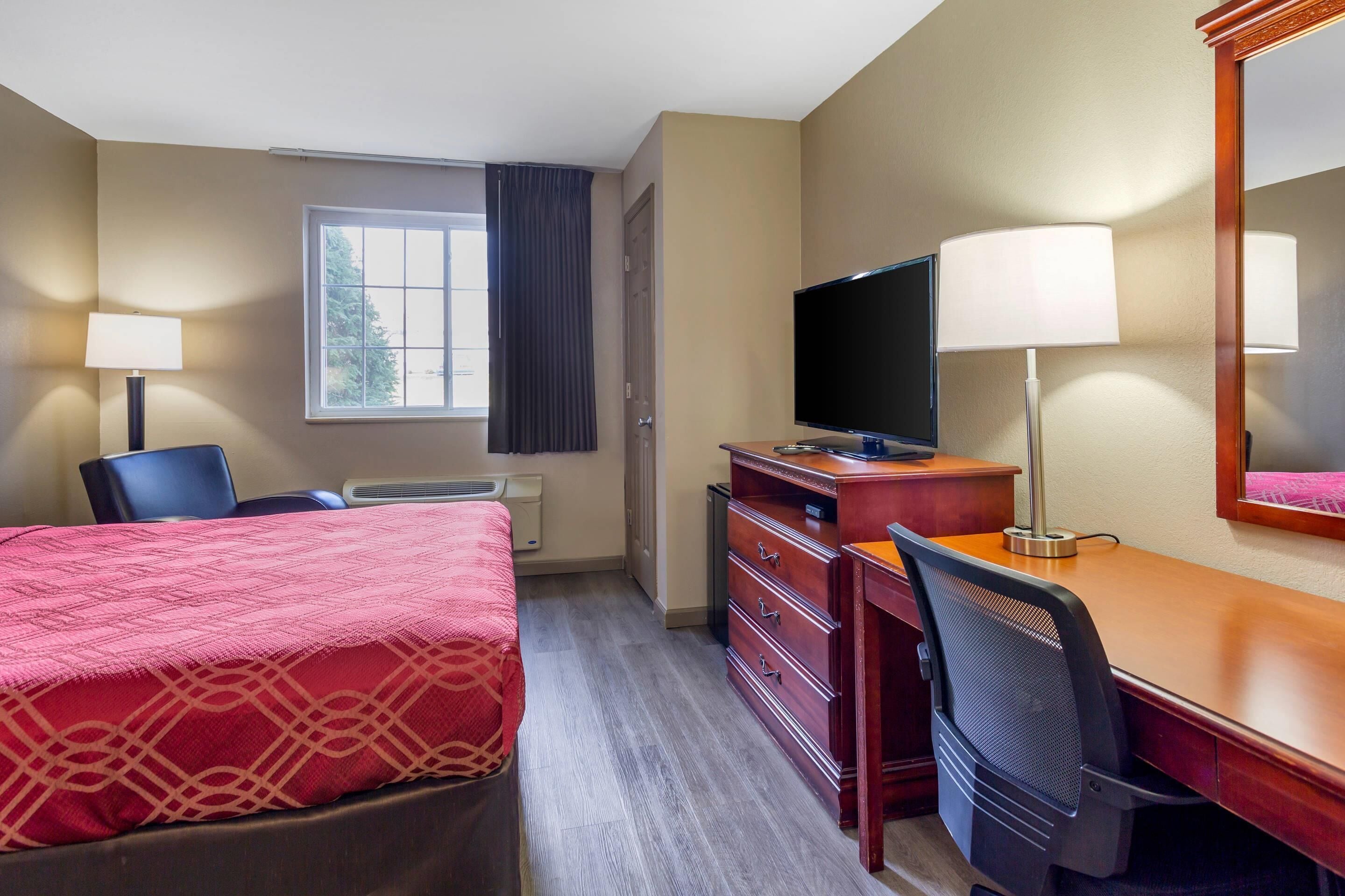 A hotel room with a bed, a desk, a television, and a chair.