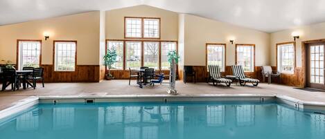 An indoor swimming pool with a view of the outside, surrounded by wooden walls and windows.