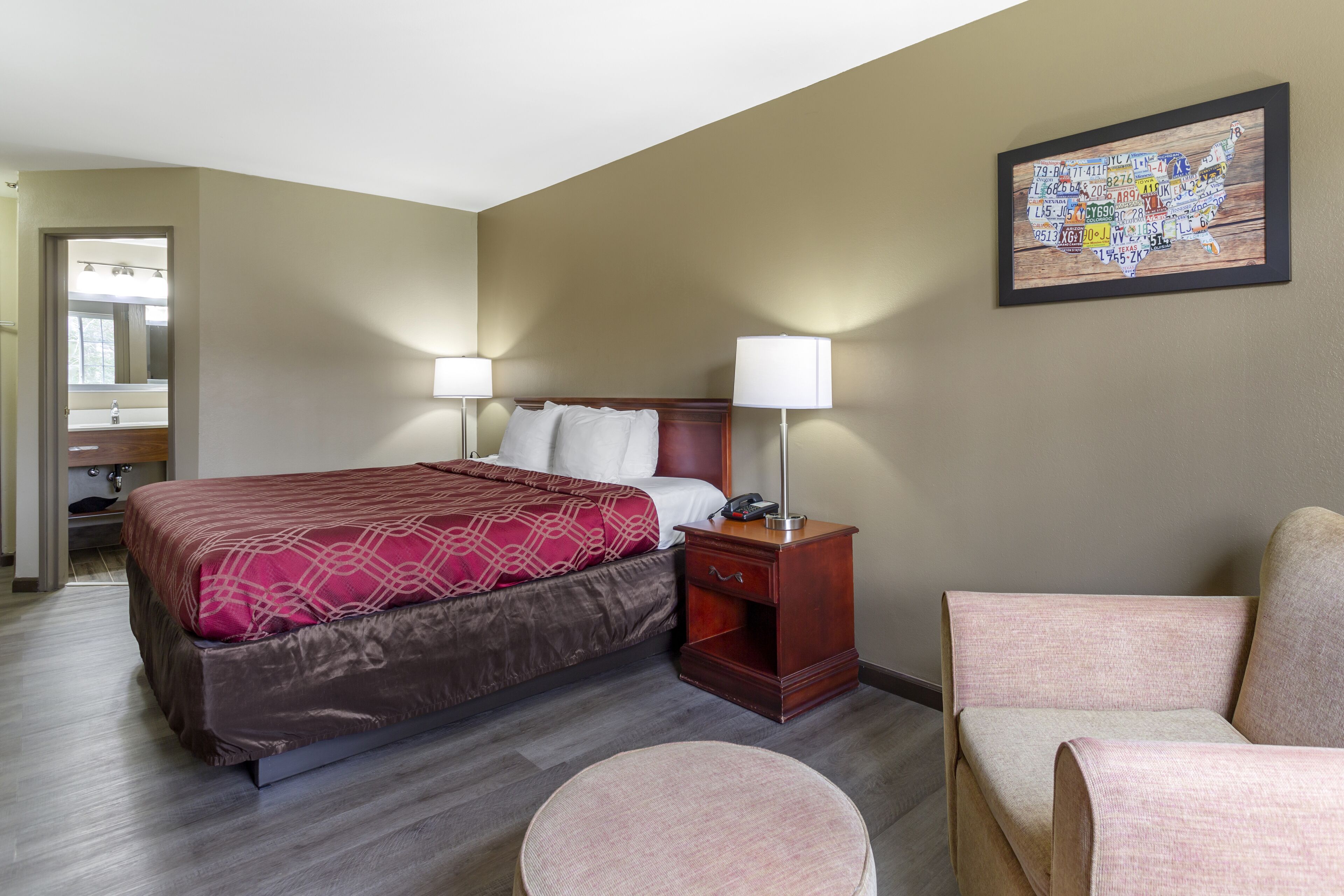 Una habitación de hotel con cama, mesita de noche, lámpara, silla y un mapa mural.