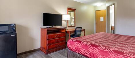 A hotel room with a bed, a desk, a television, a dresser, and a refrigerator.