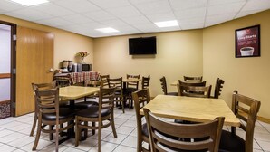 Un espace repas avec plusieurs tables et chaises, un téléviseur à écran plat fixé au mur et une affiche publicitaire pour le petit-déjeuner.