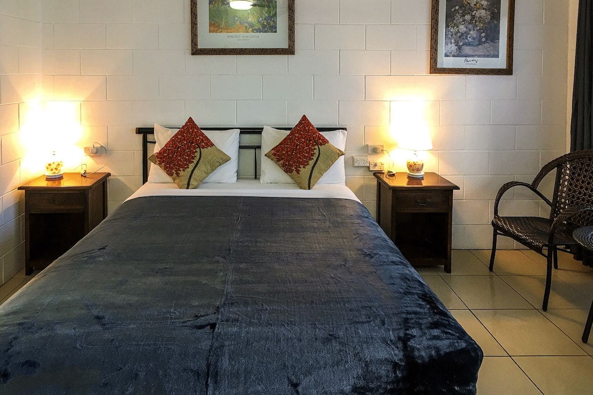 A hotel room with a bed, two nightstands, a chair, and two framed artworks on the wall.