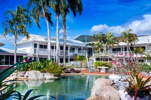 Un complexe hôtelier doté d’une piscine, de palmiers et d’un bâtiment blanc avec des balcons.
