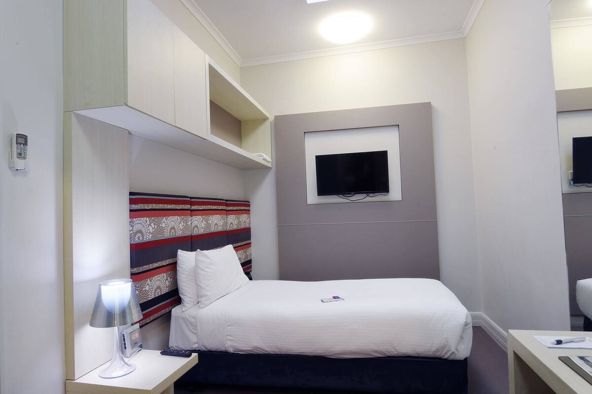 Una camera d'albergo con un letto, comodino, lampada e televisore montato a parete.
