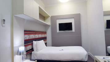 A hotel room with a bed, bedside table, lamp, and a television mounted on the wall.