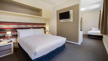 A hotel room with a large bed, a flat-screen TV mounted on the wall, a bedside table with a lamp, and a small desk with a chair.