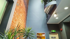 A modern lobby with a brick wall, a bookshelf, seating area, and a staircase. - Best Western Melbourne City (Melbourne)