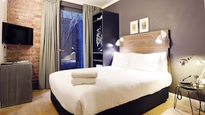 A modern hotel room with a brick accent wall, a large bed with white linens, a flat-screen TV on a wooden stand, and a nightstand with a lamp. - Best Western Melbourne City (Melbourne)
