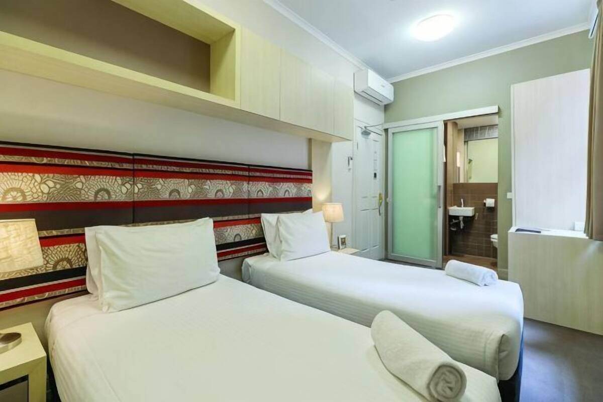 Una camera d'albergo con due letti, una scrivania, uno specchio, un armadio e un bagno.