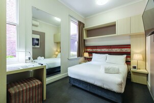 Une chambre d’hôtel avec un lit, un bureau, une chaise, une télévision et une fenêtre avec des rideaux.
