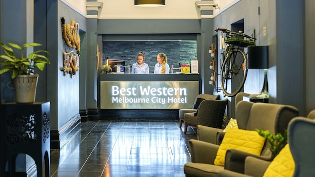 A reception area with a reception desk, two staff members, a bicycle, and seating area. - Best Western Melbourne City (Melbourne)