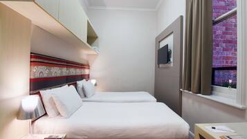 A hotel room with two beds, a desk, a lamp, a TV, and a window with curtains.