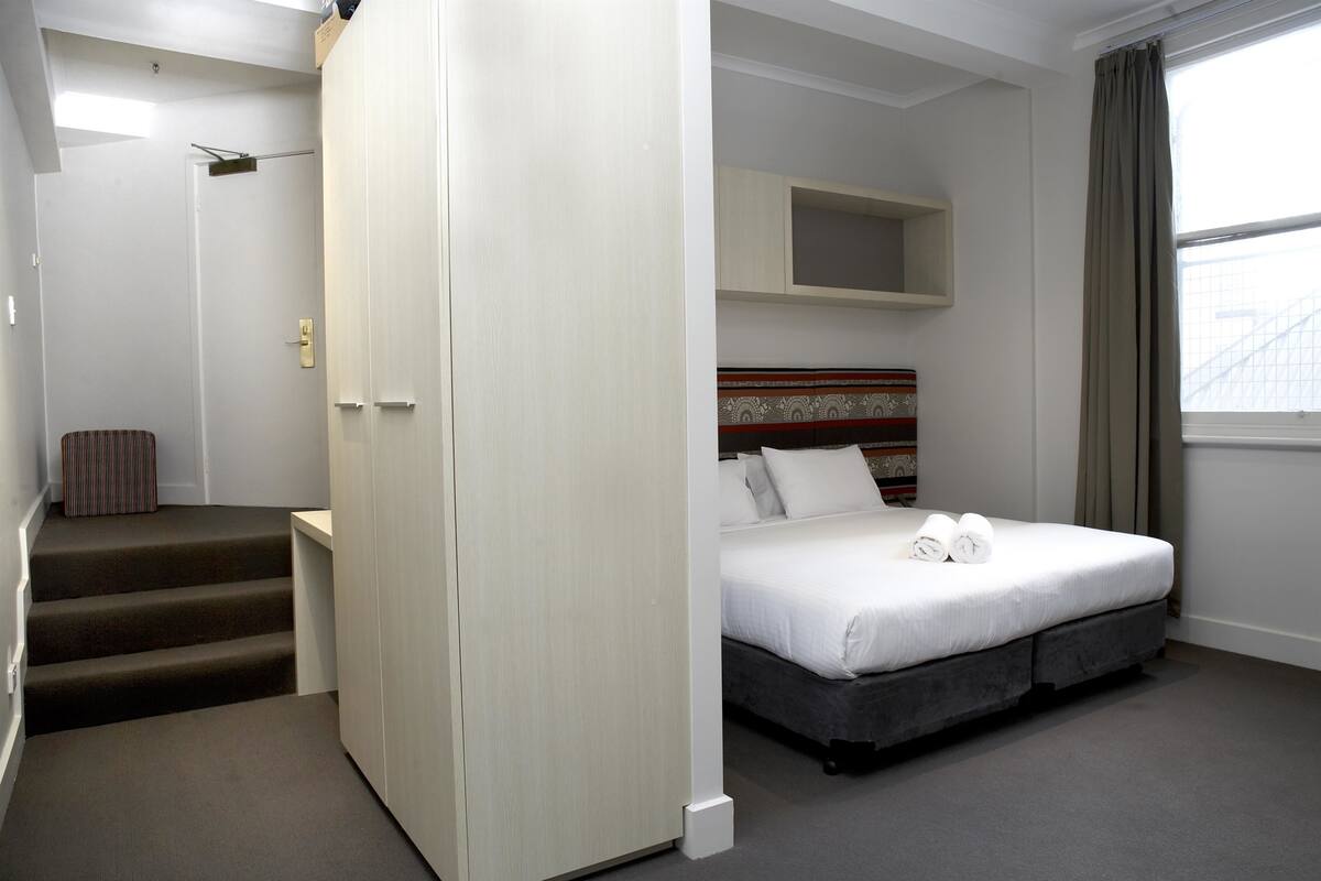 Una camera d'albergo con un letto, un armadio, un piccolo angolo salotto e una finestra.