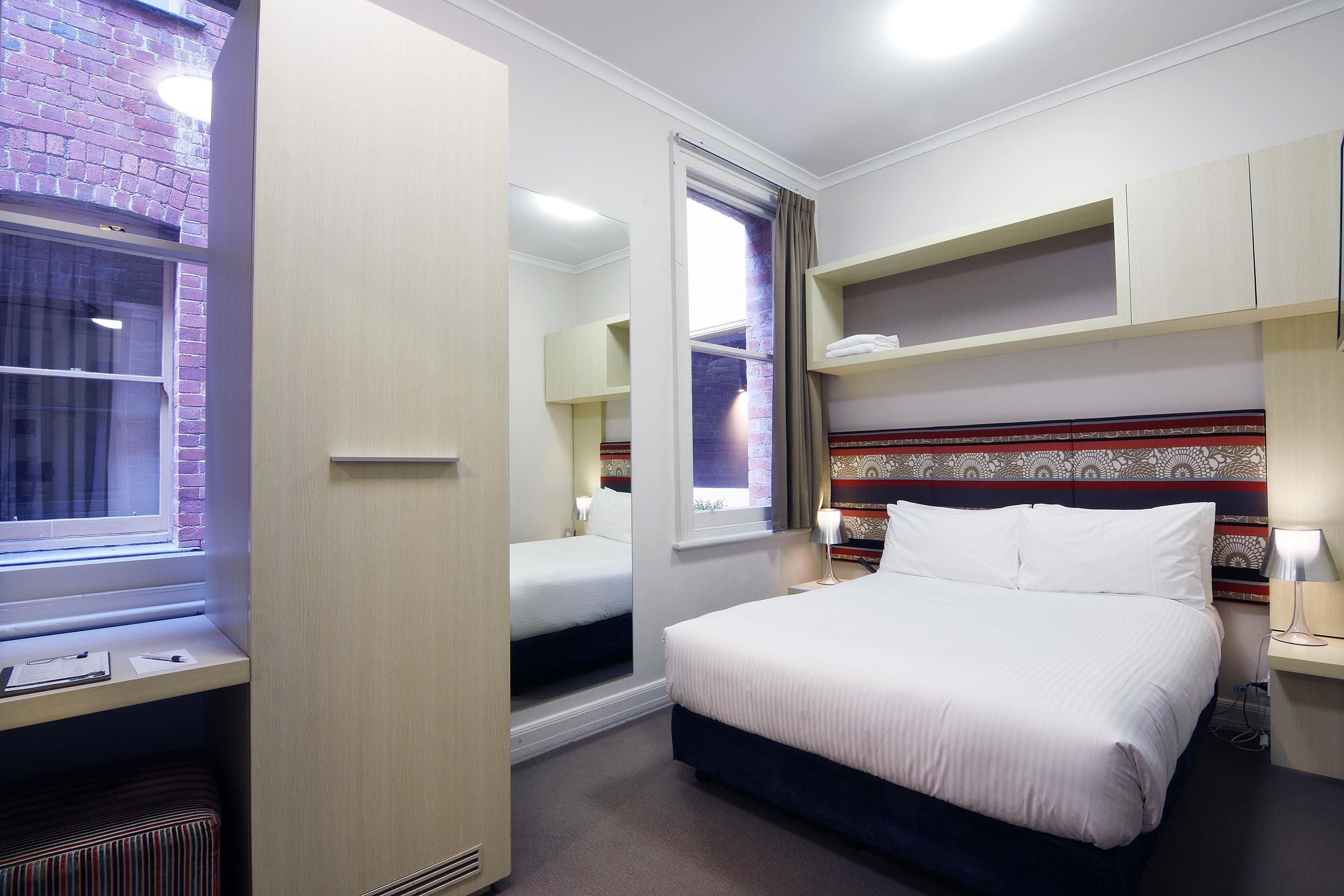 A hotel room with a large bed, a desk, and a window with a view of a brick building.