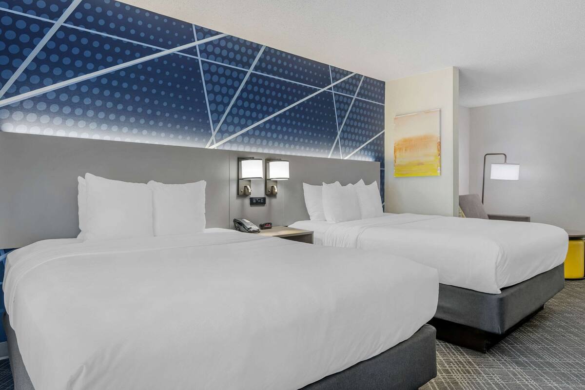 Habitación de hotel con dos camas, una mesita de noche, un teléfono y una pared con un diseño geométrico.