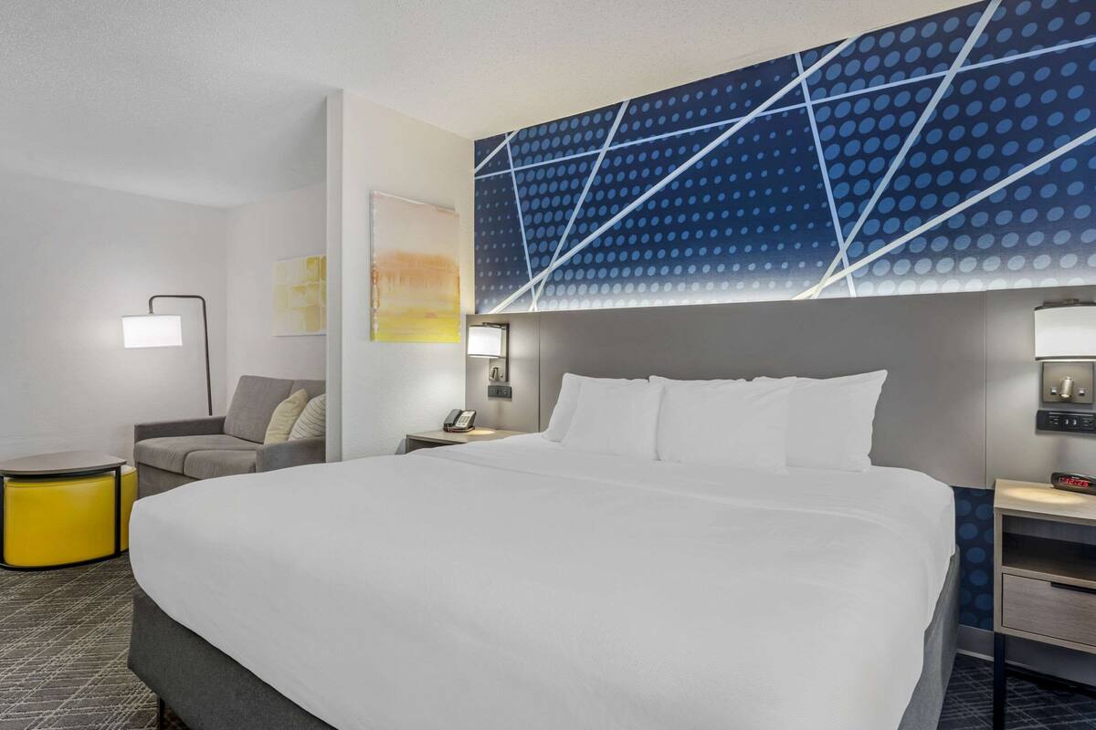 Una habitación de hotel con una cama grande, una mesita de noche con lámpara, una pequeña mesa con lámpara y una pared con diseño geométrico.