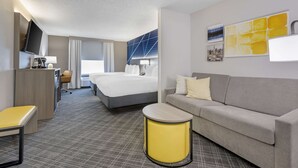 Quarto de hotel com cama, sofá, escrivaninha, cadeira e televisão.