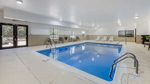 Piscina interna com água cristalina, cercada por espreguiçadeiras e uma tela de televisão.