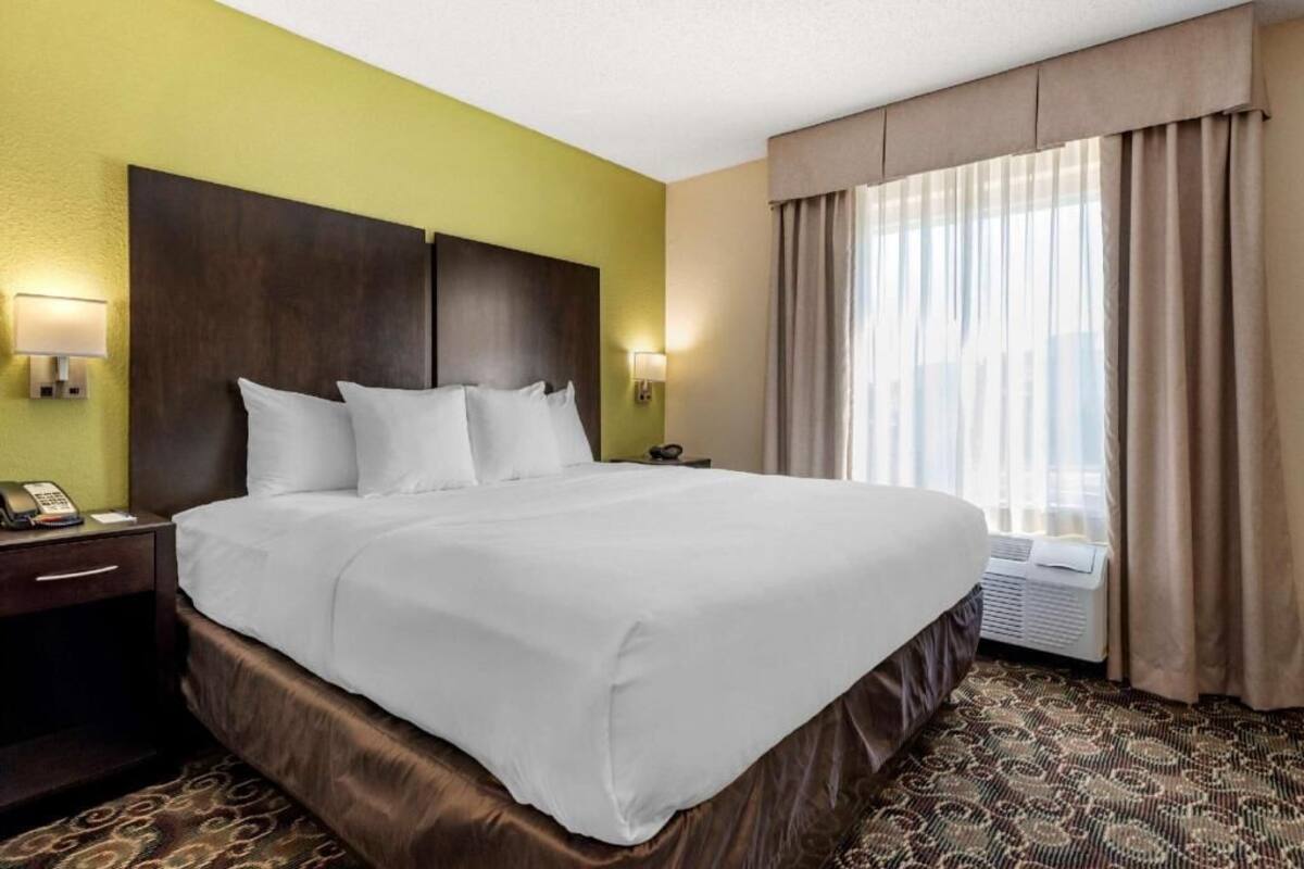 Habitación de hotel con una cama grande, teléfono en la mesita de noche, una mesita auxiliar y una ventana con cortinas.