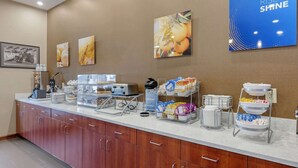 Uma mesa de pequeno-almoço com diversas opções de comida, uma máquina de café e um dispensador de água.