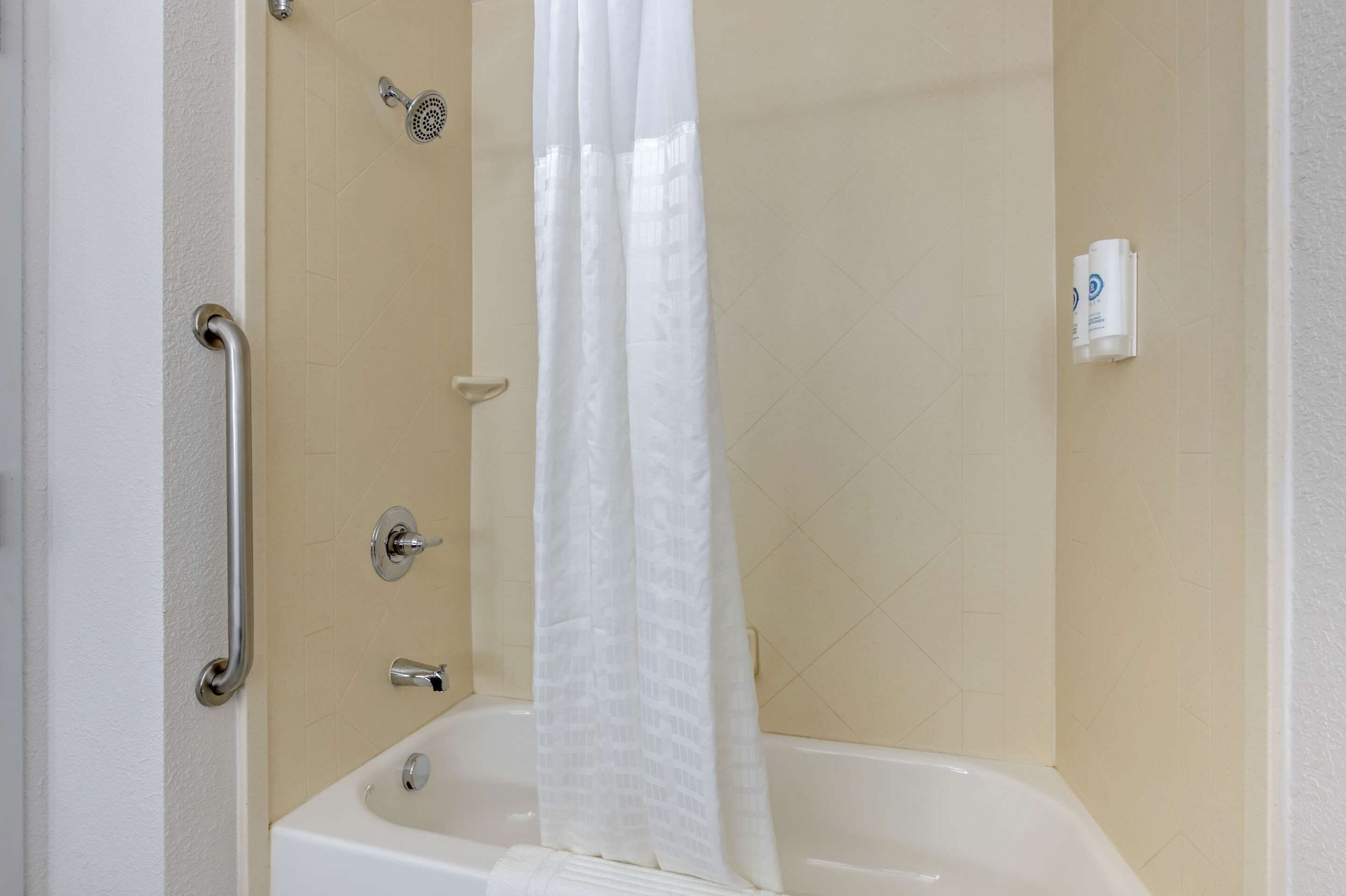 A bathroom with a bathtub, a shower, and a handrail.