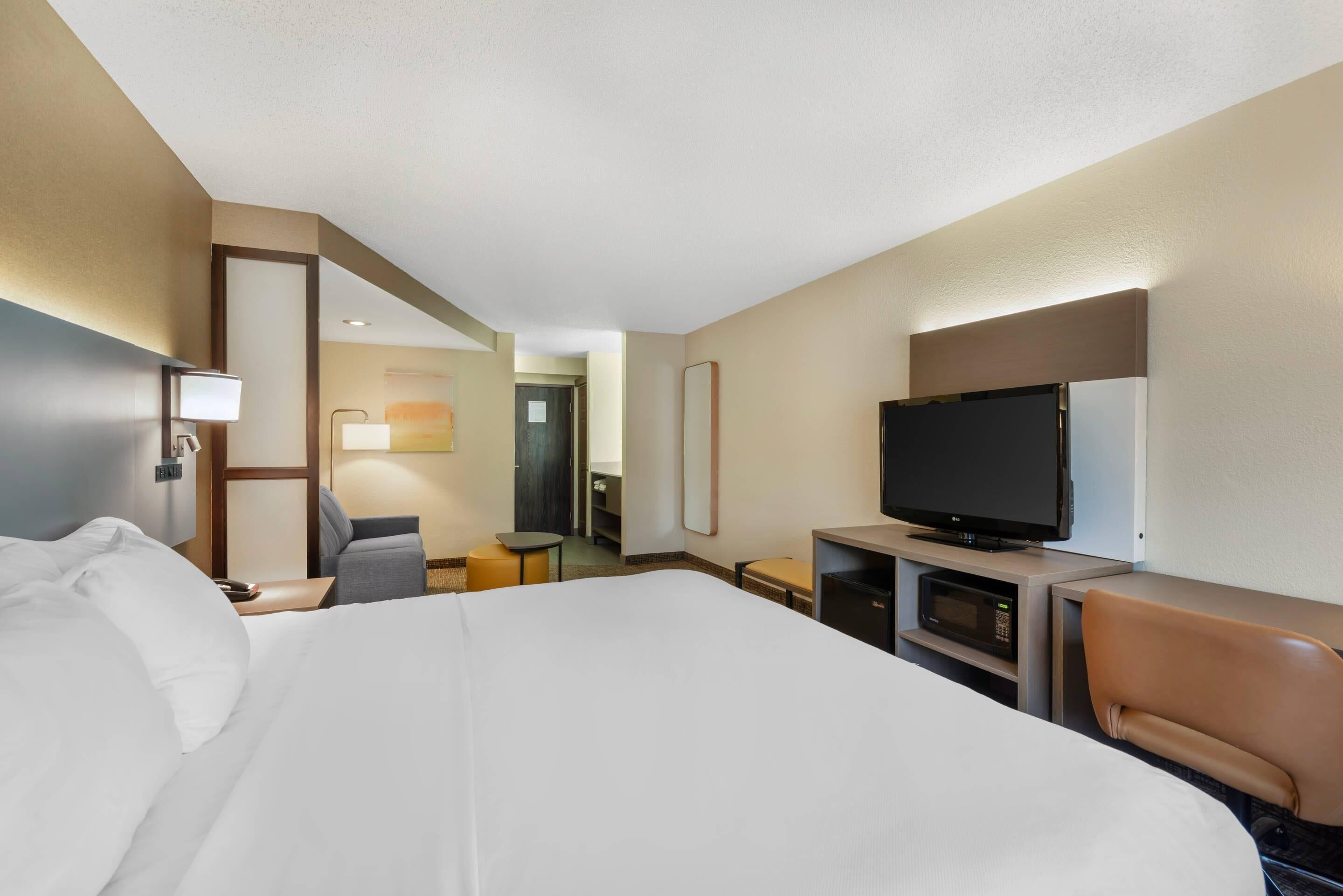 Habitación de hotel con una cama grande, un escritorio con televisión de pantalla plana, una silla, una mesita y un microondas.