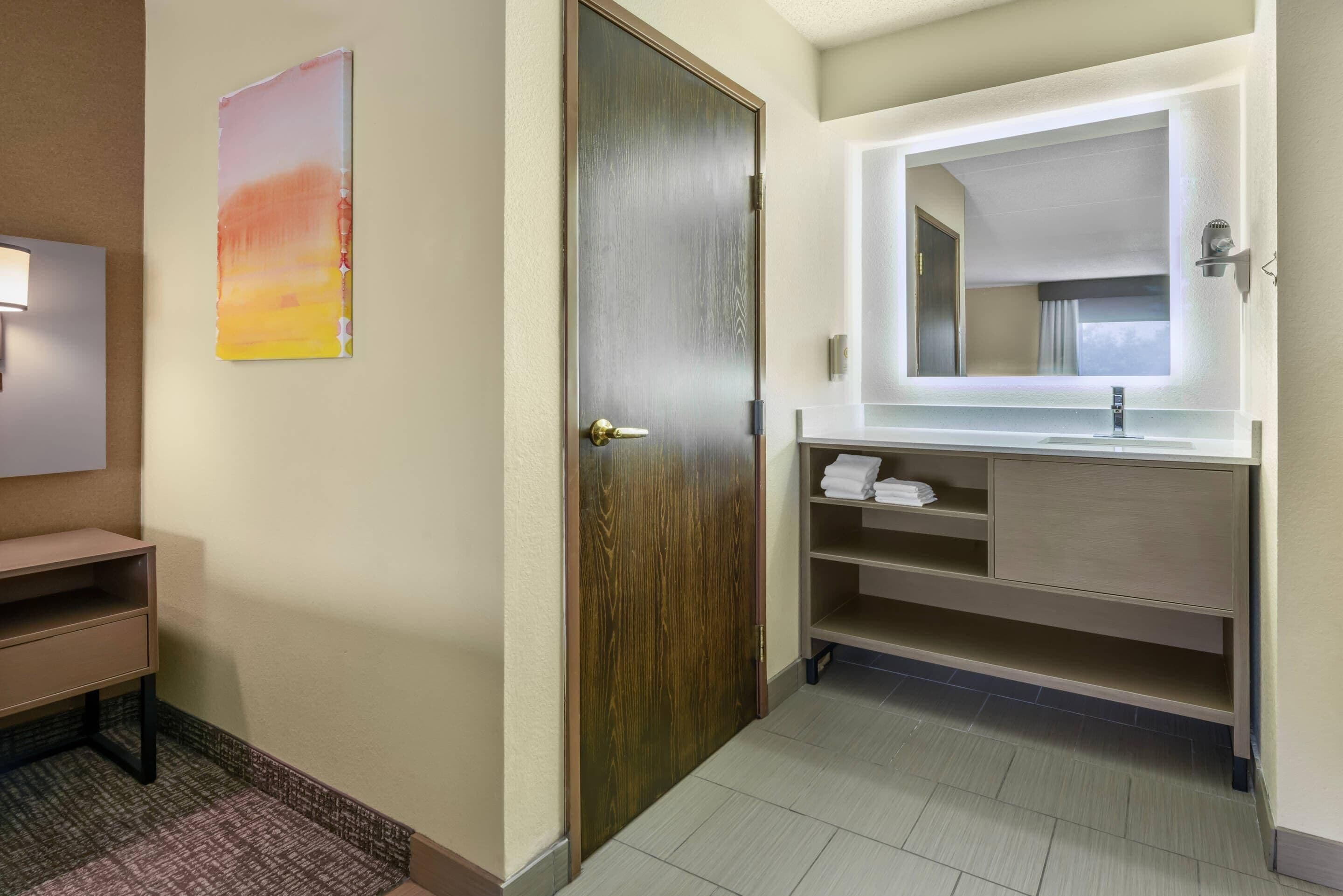 Un baño de hotel con puerta de madera, un lavabo con espejo y un perchero para toallas.