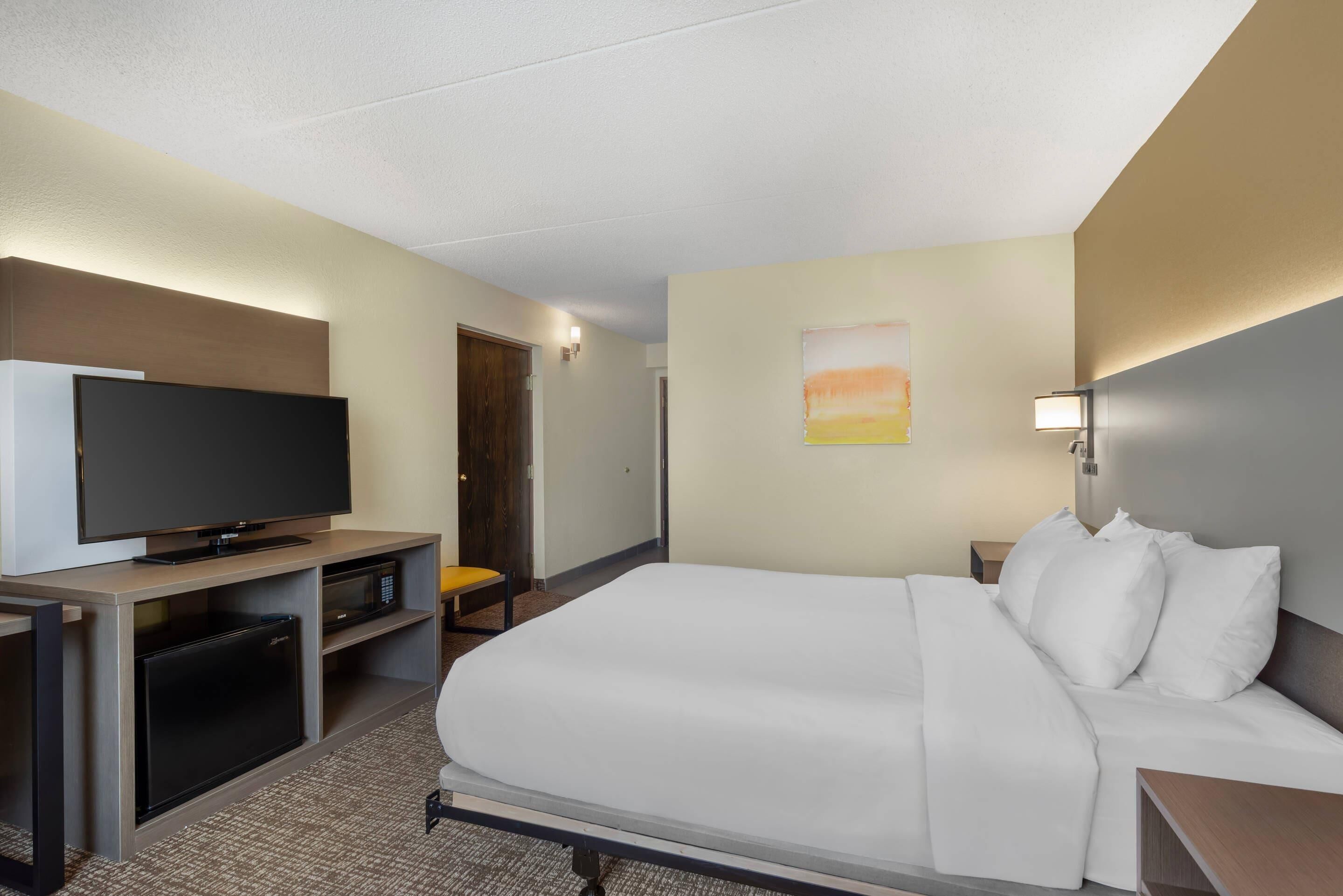 A hotel room with a bed, a television, a desk with a microwave, and a door.