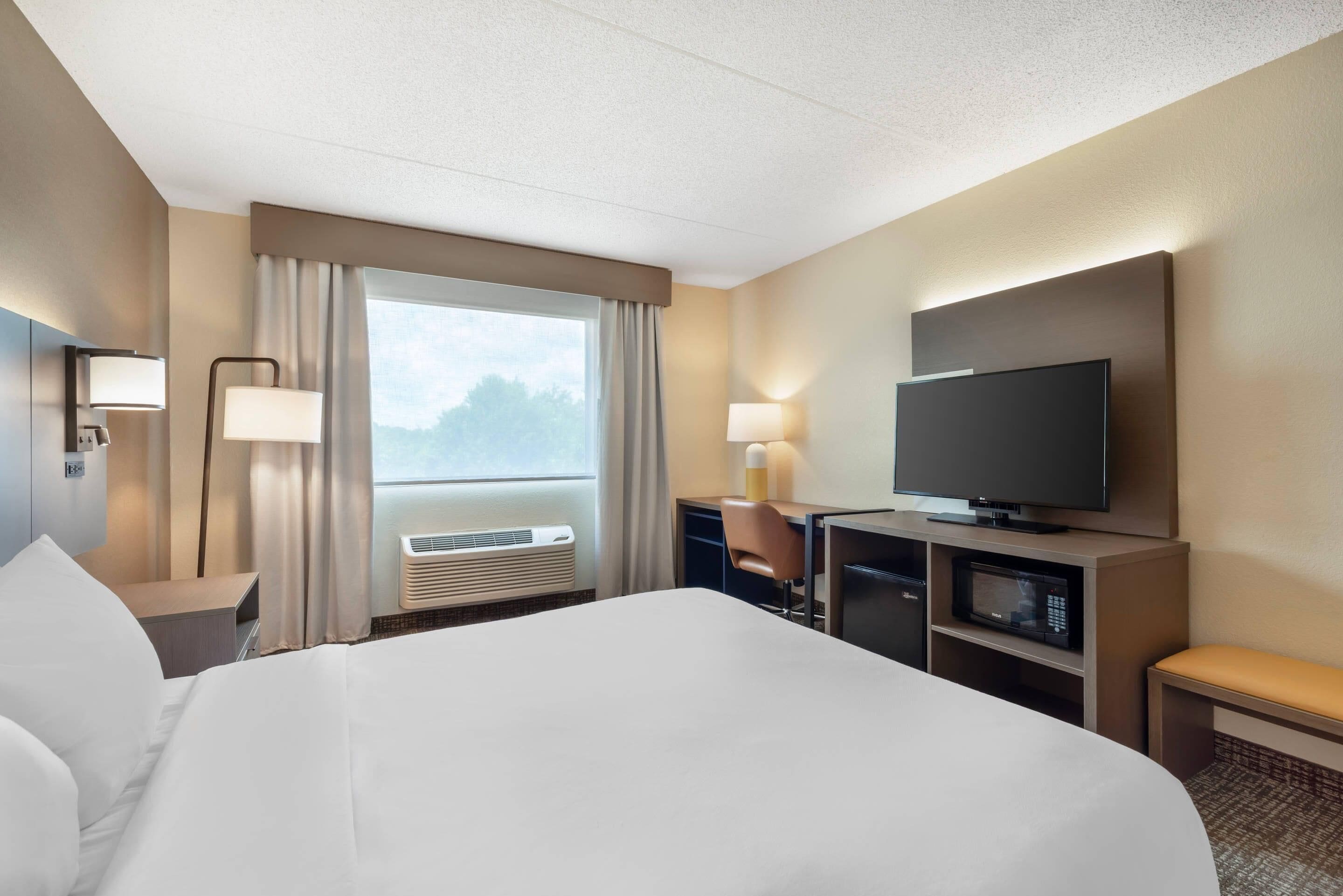 Une chambre d’hôtel avec un grand lit, un bureau avec une chaise, une télévision et une fenêtre avec des rideaux.