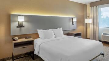 Una habitación de hotel con una cama grande, mesitas de noche, una lámpara y una ventana con cortinas.