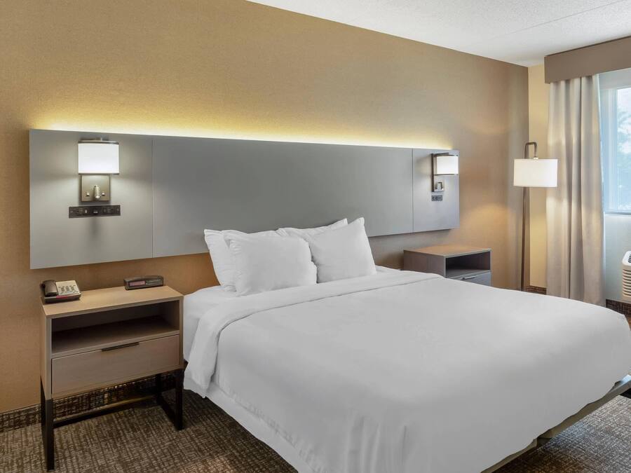 A hotel room with a large bed, bedside tables, a nightstand, a lamp, and a window with curtains.