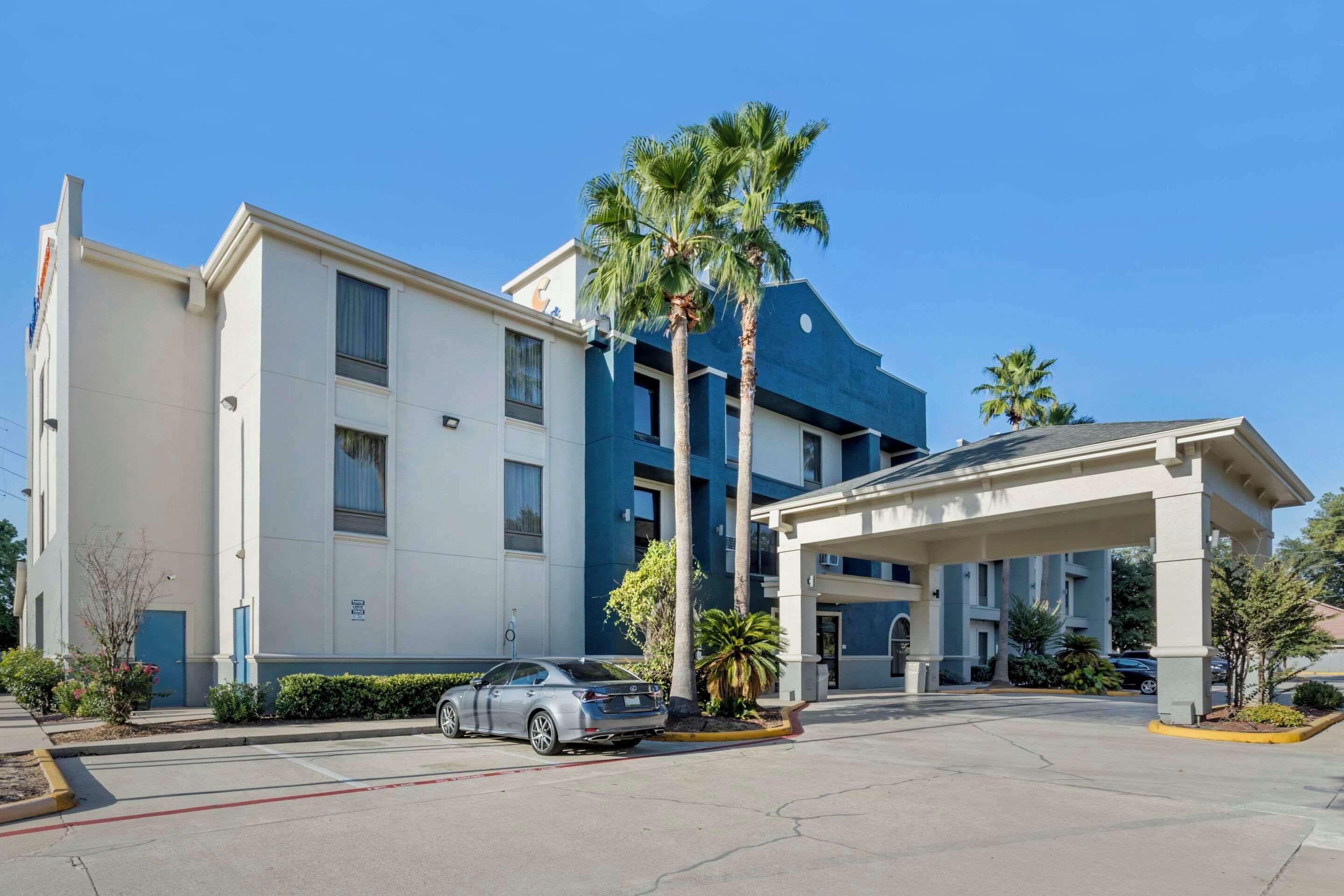 A hotel with a covered entrance, a car parked in front, and palm trees.