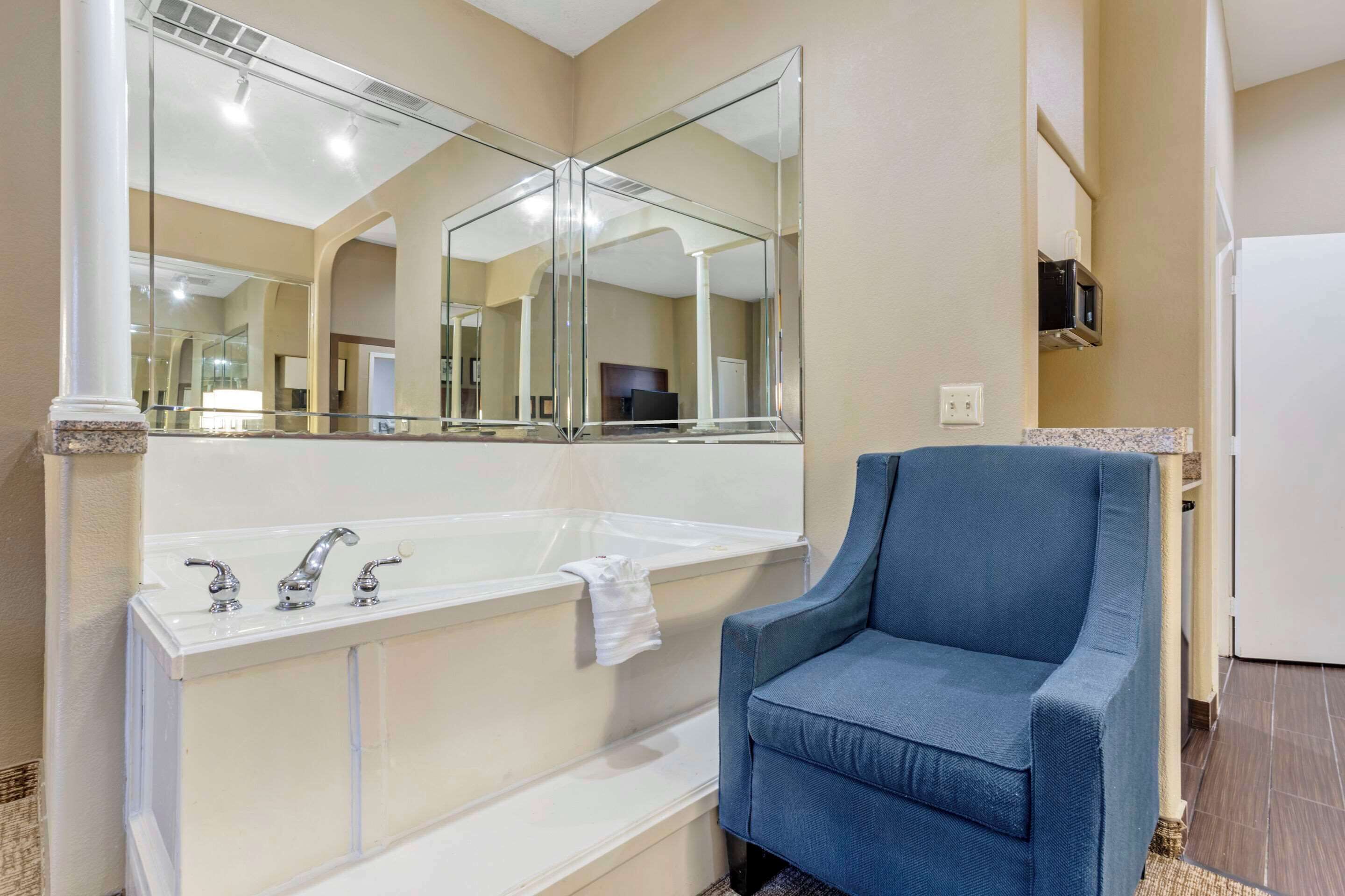 A bathroom with a large mirror, a bathtub, and a blue chair.