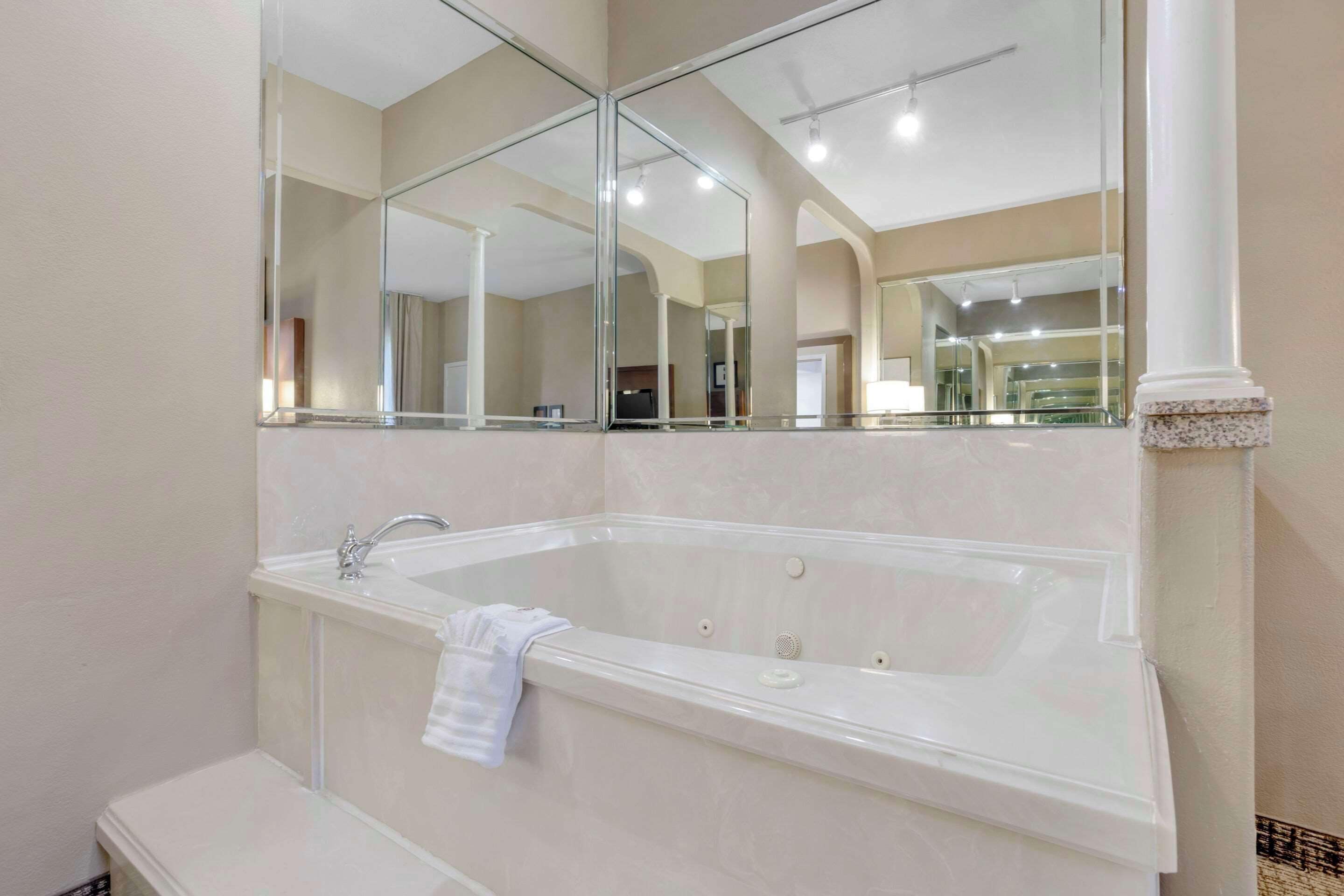 Een moderne badkamer met een vrijstaand ligbad, een spiegel erboven en een bankje.