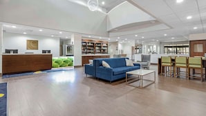 A spacious lobby with a reception desk, a blue sofa, a dining area, and a kitchen in the background.