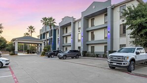 A multi-story hotel with a covered entrance, parking lot, and several vehicles parked in front.