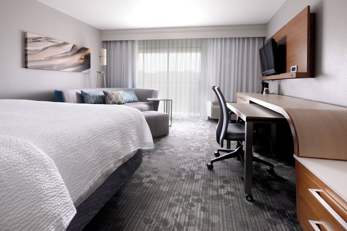 A hotel room with a large bed, a desk, a chair, a television, and a window with curtains.