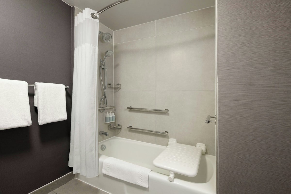 A modern bathroom with a bathtub, shower, and grab bars.