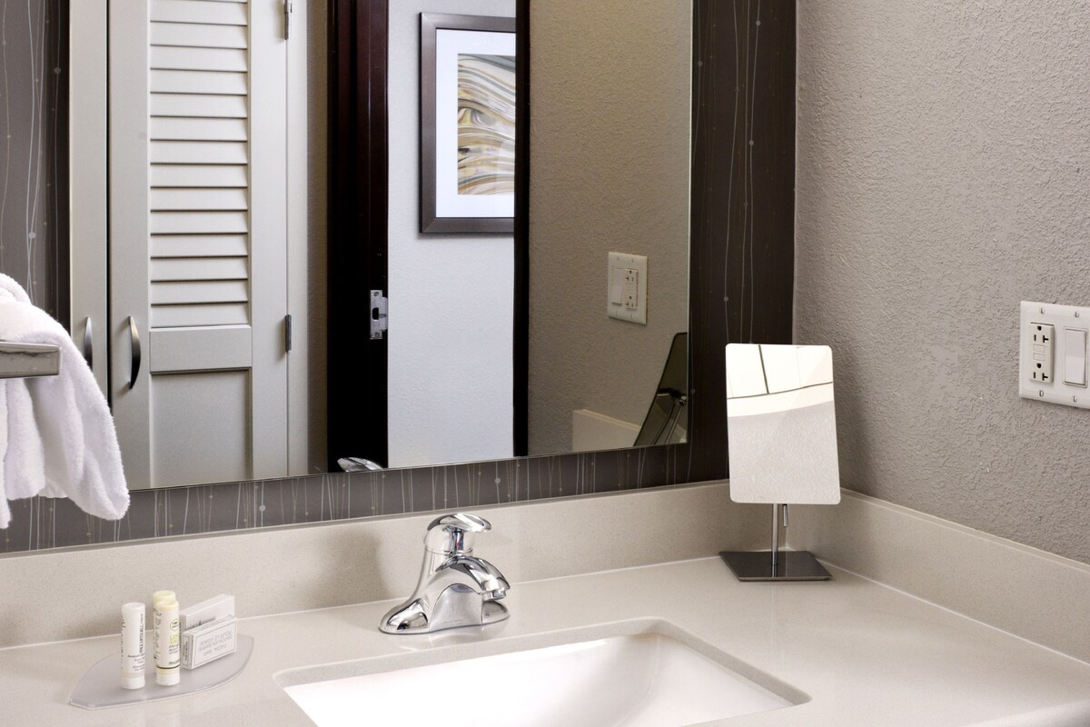 A hotel bathroom with a white sink, a mirror, and a towel rack.