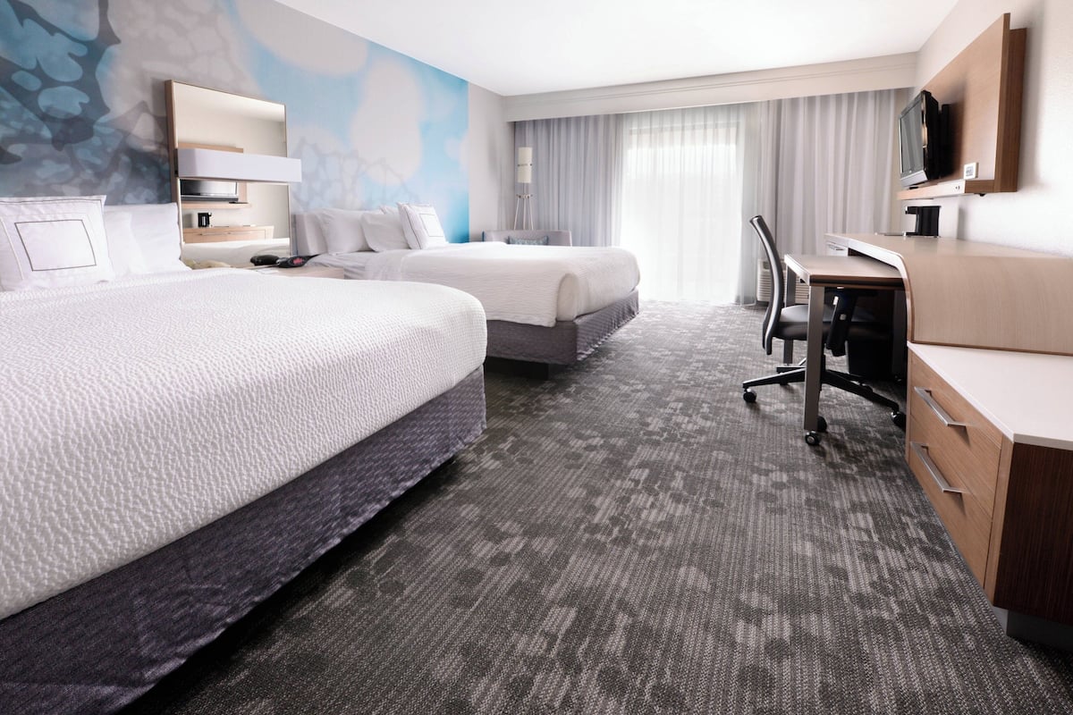 A hotel room with two beds, a desk, a chair, a television, and a large window with curtains.